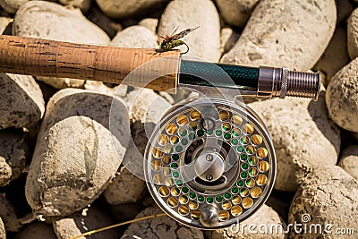 A close up of a trout fly rod, reel and line on rocks, with a cicada fly Stock Photo