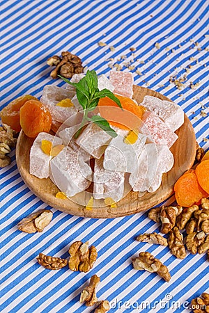 Close-up of turkish delight, dried apricots, bright leaves of mint and walnuts on a striped background, top view. Stock Photo