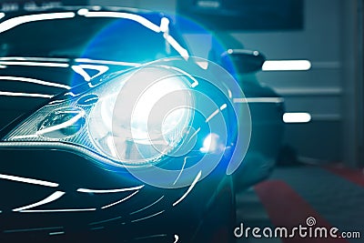 Close up of turned on headlight of sports car parked inside garage. Lens flare. Car maintenance concept. Indoor Stock Photo