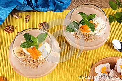 Close-up of two banana smoothies in dessert glasses, Turkish Delight and dried apricots with walnuts on a colored Stock Photo