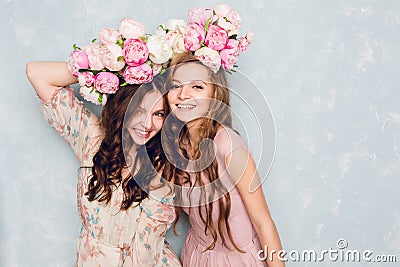 Close-up of two beautiful girls stand in a studio,who play silly with circlets of flowers on their heads. They wear Stock Photo