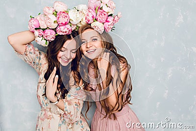 Close-up of two beautiful girls stand in a studio,who play silly with circlets of flowers on their heads. They wear Stock Photo