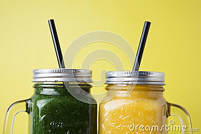 Close up two jars with green and yellow detox smoothie with straws. Spinach and pumpkin smoothie on wooden table Stock Photo