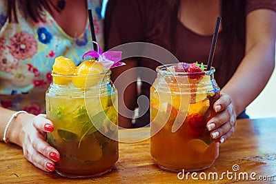 Close up of two women in colourful dresses holding glasses with refreshing strawberry apple cocktail with lime and peach Stock Photo