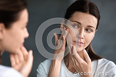 Close up unhappy woman looking at acne spots in mirror Stock Photo