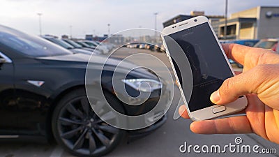 CLOSE UP: Unknown person holds a smartphone and steers car out of parking space. Editorial Stock Photo
