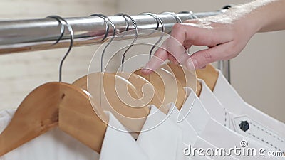 Close-up van de hand van een vrouw die een wit overhemd kiezen van een verscheidenheid van kleren die op de hanger hangen stock footage Close-up van de hand van een vrouw die een wit overhemd kiezen van een verscheidenheid van kleren die op de hanger hangen stock footage