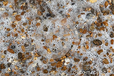 A close up of various coloured and size pebbles on a beach that are partly covered in water with lots of bubbles Stock Photo