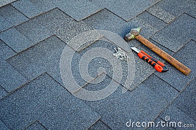 Close up view on asphalt bitumen shingles on a roof with hammer,nails and stationery knife background. Stock Photo