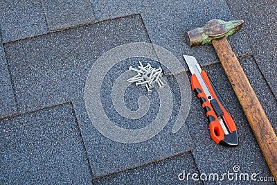 Close up view on asphalt bitumen shingles on a roof with hammer,nails and stationery knife background. Stock Photo