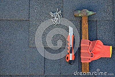 Close up view on asphalt shingles on a roof with hammer,nails and knife. Use of gloves in construction. Stock Photo