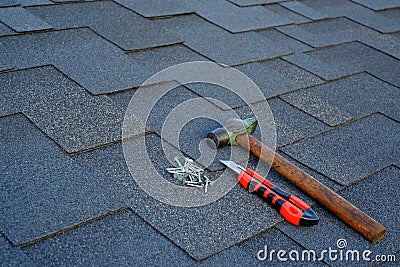 Close up view on asphalt shingles on a roof with hammer,nails and stationery knife background Stock Photo