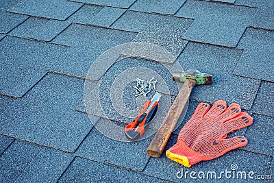 Close up view on asphalt shingles on a roof with hammer,nails and stationery knife. Stock Photo