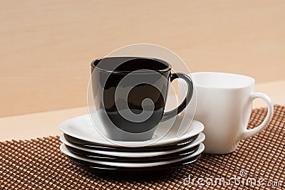 Close up view of black tea cup on the stack of the white and black plates near white tea cup on tablemat. Stock Photo