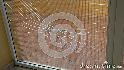 Close-up view of broken windowpane with a wire mesh behind it. Glass is shattered with numerous cracks, creating web-like pattern. Stock Photo