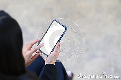 Businesswoman holding mock up smart phone with blank screen while sitting at outdoor office. Stock Photo