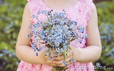 Close up view of child in pink party dress holding bouquet of Myosotis also known as forget me nots or scorpion grasses. Stock Photo