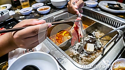 The close up view of chopstick holding a slice of raw meat before dip into the boiling soup Stock Photo