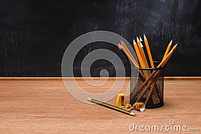 close up view of desk organizer with pencils and sharpener on wooden table in front of empty chalk board Stock Photo