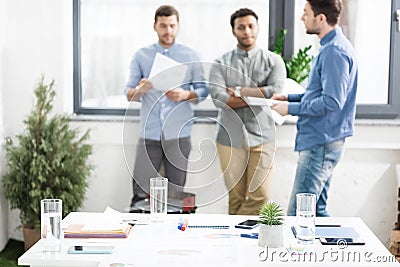 Close-up view of documents and business charts on desk and businessmen standing behind Stock Photo