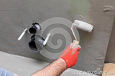 A close-up view of an experienced construction worker applying damp insulation using a paint roller on a wall Stock Photo