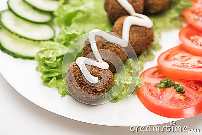 Close up view of falafel with sauce on plate with sliced vegetables on white background. Stock Photo