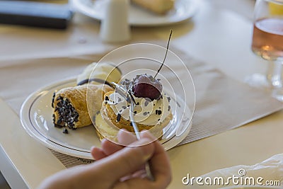 Close up view of female hand with tea spoon taking cherry from top of cake. Stock Photo