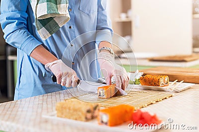 Close-up view of female hands in gloves cooking traditional Japanese sushi rolls cutting with knife in kitchen Stock Photo