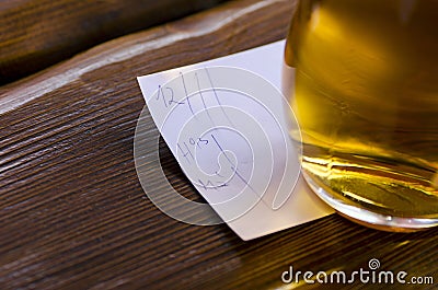 Close-up view of a glass of beer with a bill lying on a table in Stock Photo