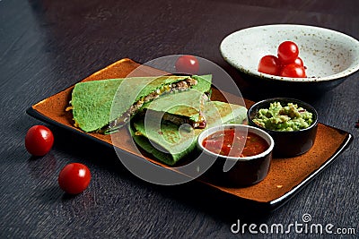 Close up view green tortilla quesadilla with chicken, cheese on a brown plate with red sauce on a wooden background. mexican Stock Photo