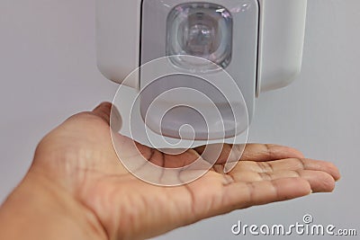 Close-up view of hand under an automatic wall mounted sanitiser dispenser. Stock Photo