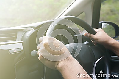 view of human hands holding steering wheel driving a car on a city street on a mist sunny day Stock Photo
