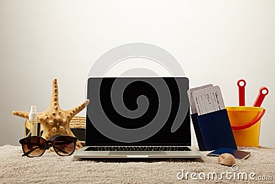 close up view of laptop with blank screen, sea star, sunglasses, passports with tickets and toy bucket on sand on grey background Stock Photo