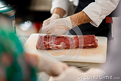 Close-up view of meat and chef hands which tie it with butcher& x27;s twine Stock Photo