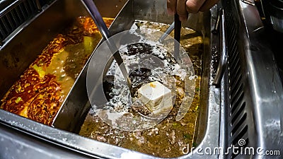 The close up view of a metal ladle dipping a cold tofu into a boiling soup Stock Photo