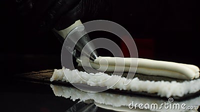 Close-up view of process of preparing roll sushi. Chef in gloves imposes from pastry bag of cream filling on sheet of Stock Photo
