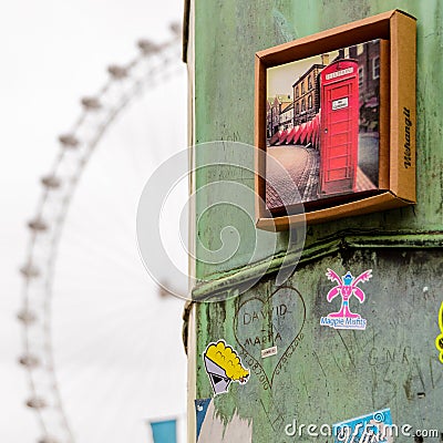 Close up view of a rusty metal column with stickers and a red phone booth photo on it with the London Eye on the background. Editorial Stock Photo