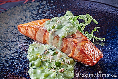 Close up view on Salmon steak in dark facture plate served with green sauce. Selective focus on Fish meal. Cooked salmon steak for Stock Photo