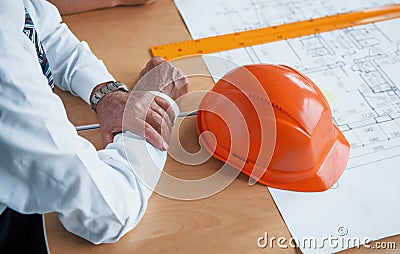 Close up view of senior businessman hands, hard hat and architect project on the table Stock Photo