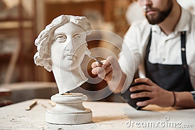 Skillful sculptor makes professional restauration of gypsum sculpture of woman`s head at the creative workshop. Stock Photo