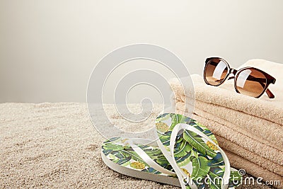 close up view of stack of towels, sunglasses and summer flip flops on sand on grey backdrop Stock Photo