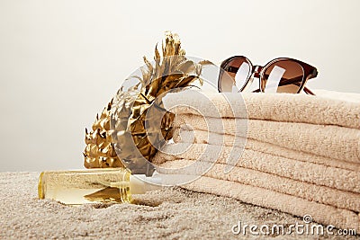 close up view of stack of towels, sunglasses, tanning oil and golden decorative pineapple on sand on grey backdrop Stock Photo