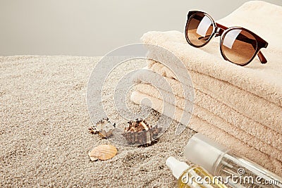 close up view of stack of towels, sunglasses, tanning oil and seashells on sand on grey background Stock Photo