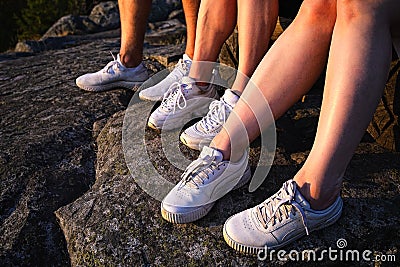 Close up view of three pairs of legs in white sneakers in nature at sunset Stock Photo