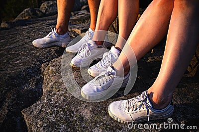 Close up view of three pairs of legs in white sneakers in nature at sunset Stock Photo