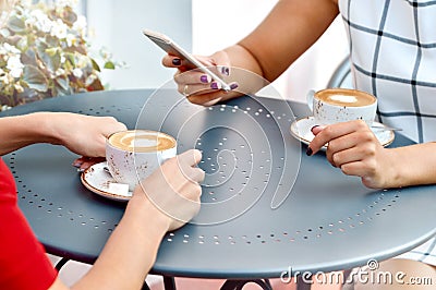 Two coffee cups and hands of young women with smartphone at outdoor cafe Stock Photo