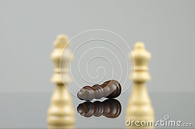 Close-up view of two wooden white chess pieces defeating a black chess king with a reflection Stock Photo