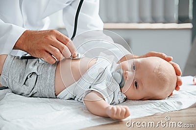 Close up view. Using stethoscope. Doctor in white coat is taking care of little toddler indoors Stock Photo