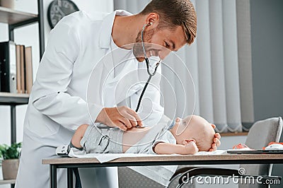 Close up view. Using stethoscope. Doctor in white coat is taking care of little toddler indoors Stock Photo