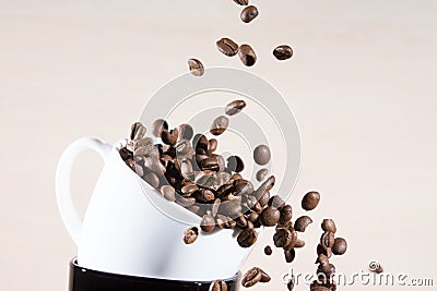 Close up view of white cup standing on black cup with falling down brown roasted coffee beans. Stock Photo